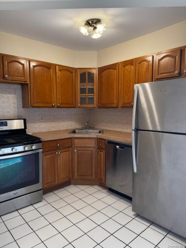150-40 Tahoe Street, Unit 3C Queens, NY 11417 - Photo 5 of 18 Kitchen with stainless steel appliances, brown cabinets, glass insert cabinets, and backsplash