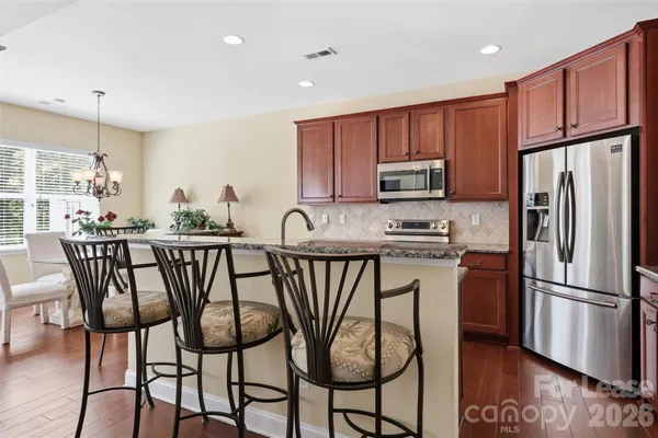 a kitchen with stainless steel appliances granite countertop a refrigerator a stove a sink and a dining table with wooden cabinet