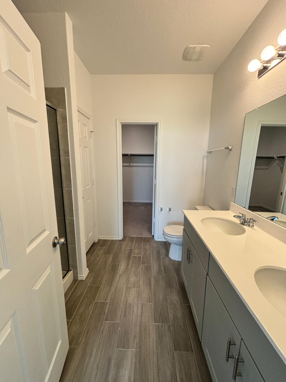 1509 Hope Rnch Road Leander, TX 78641 - Photo 14 of 25 Bathroom featuring a walk in closet, a shower stall, wood finished floors, double vanity, and a textured ceiling