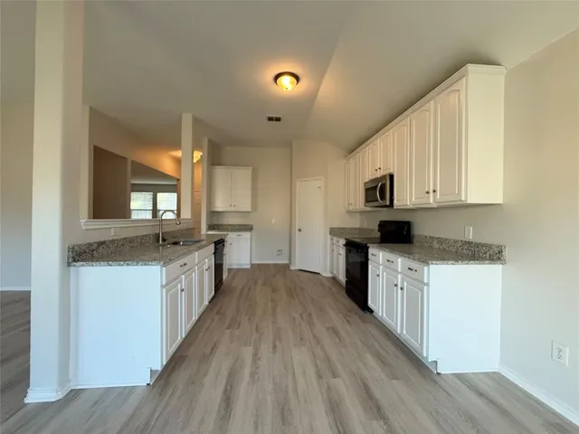 a kitchen with granite countertop a stove top oven a sink dishwasher and a refrigerator with wooden floor