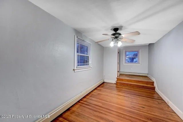 an empty room with wooden floor fan and windows