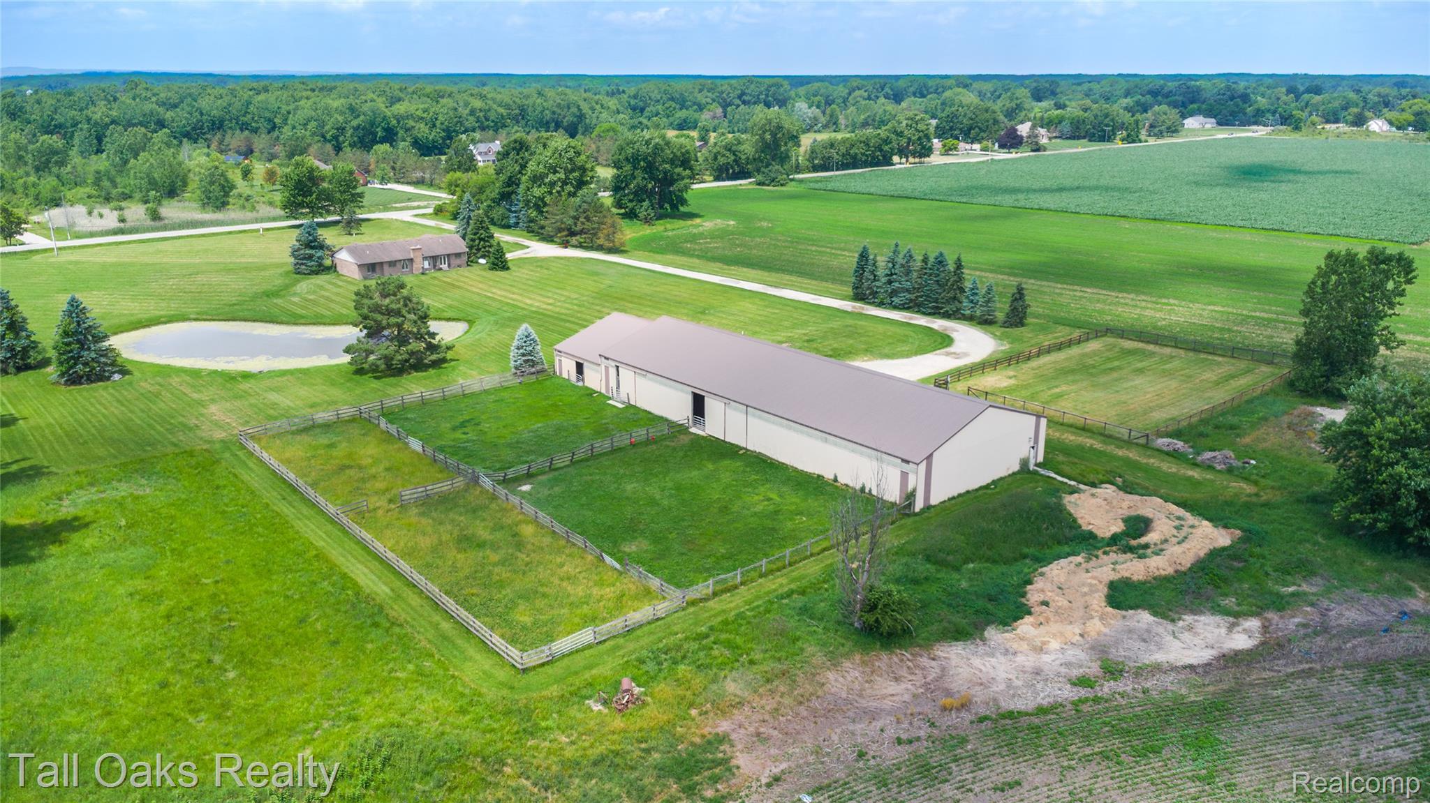 79330 Capac Road Armada, MI 48005 - Photo 5 of 42 Expansive property featuring a large metal-sided outbuilding with a brown roof, multiple fenced enclosures, a private pond, and extensive manicured green space