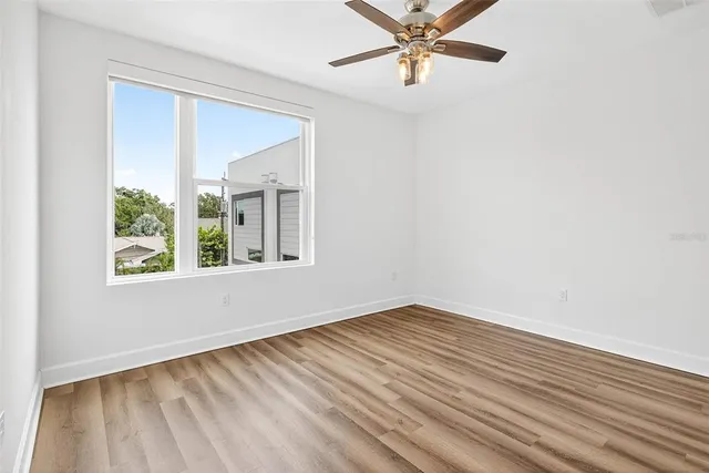 an empty room with wooden floor ceiling fan and windows