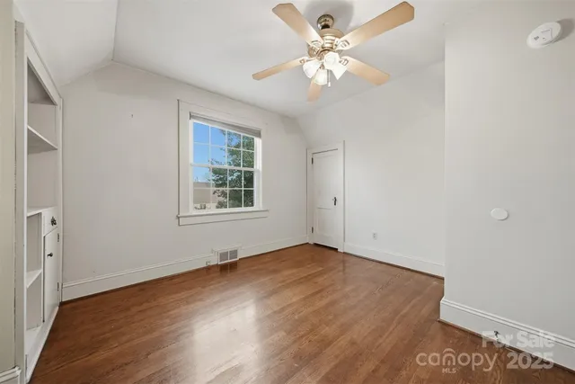an empty room with wooden floor chandelier fan and windows