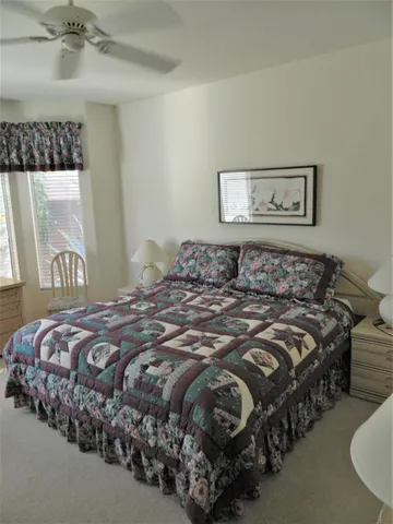 a bedroom with a bed a table chair and a large window