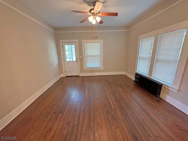 an empty room with wooden floor chandelier fan and windows