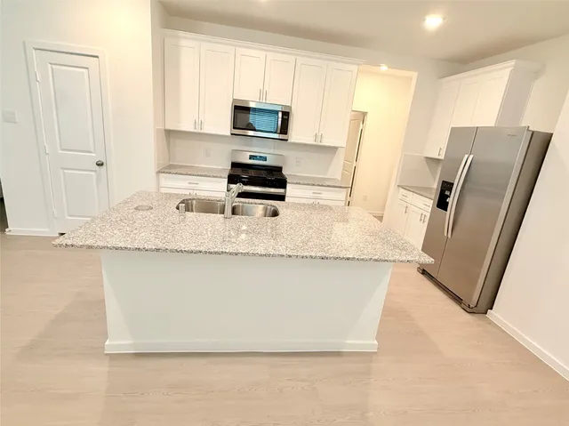 a kitchen with stainless steel appliances granite countertop a refrigerator a stove a sink a microwave a refrigerator and white cabinets with wooden floor