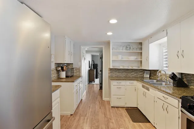 a kitchen with a sink dishwasher stove and white cabinets with wooden floor