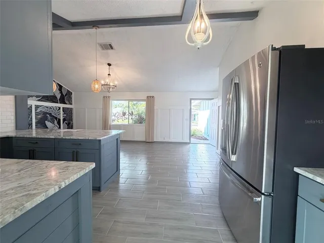 a kitchen with stainless steel appliances granite countertop a refrigerator a sink dishwasher a stove and a dining table with wooden floor