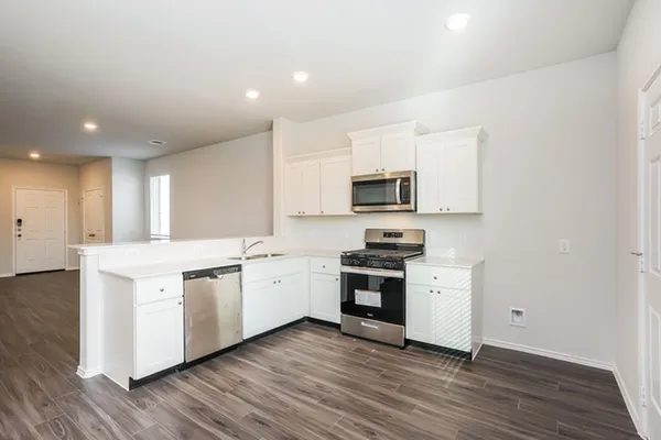 a kitchen with stainless steel appliances granite countertop a stove top oven a sink a refrigerator and white cabinets with wooden floor
