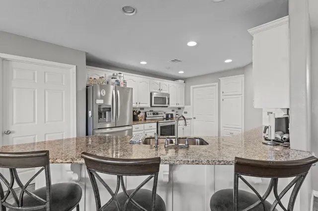 a kitchen with kitchen island granite countertop a dining table chairs cabinets and stainless steel appliances