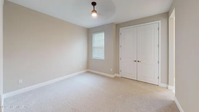an empty room with chandelier fan and windows