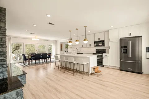 a kitchen with stainless steel appliances kitchen island granite countertop a refrigerator a stove a dining table and chairs with wooden floor
