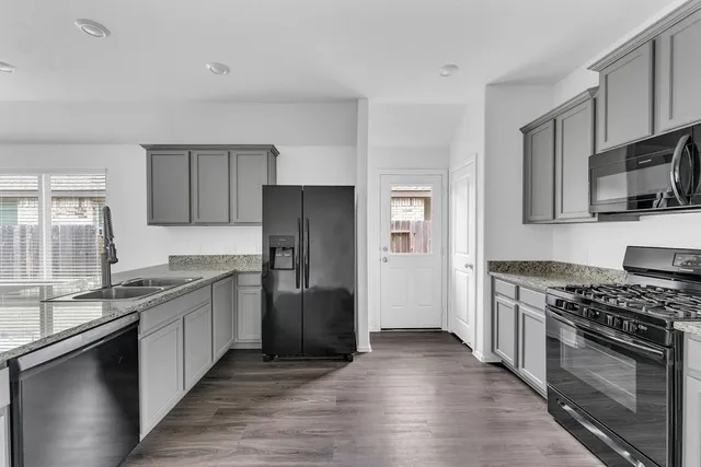 a kitchen with stainless steel appliances granite countertop a stove top oven a sink dishwasher a refrigerator and a microwave oven with wooden floor