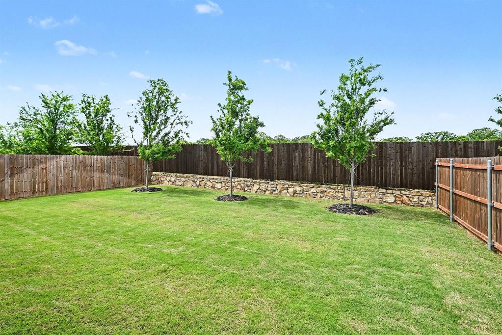 513 Bronze Circle West Springtown, TX 76082 - Photo 23 of 25 Expansive backyard featuring a manicured lawn, full privacy fencing, and a stone retaining wall