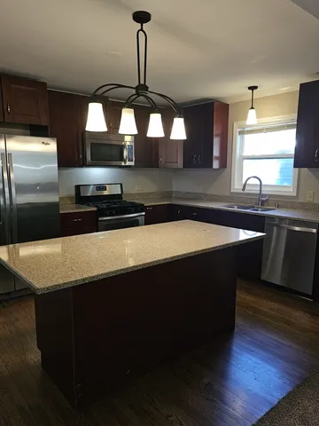 a kitchen with stainless steel appliances a sink a stove a refrigerator white cabinets and wooden floor