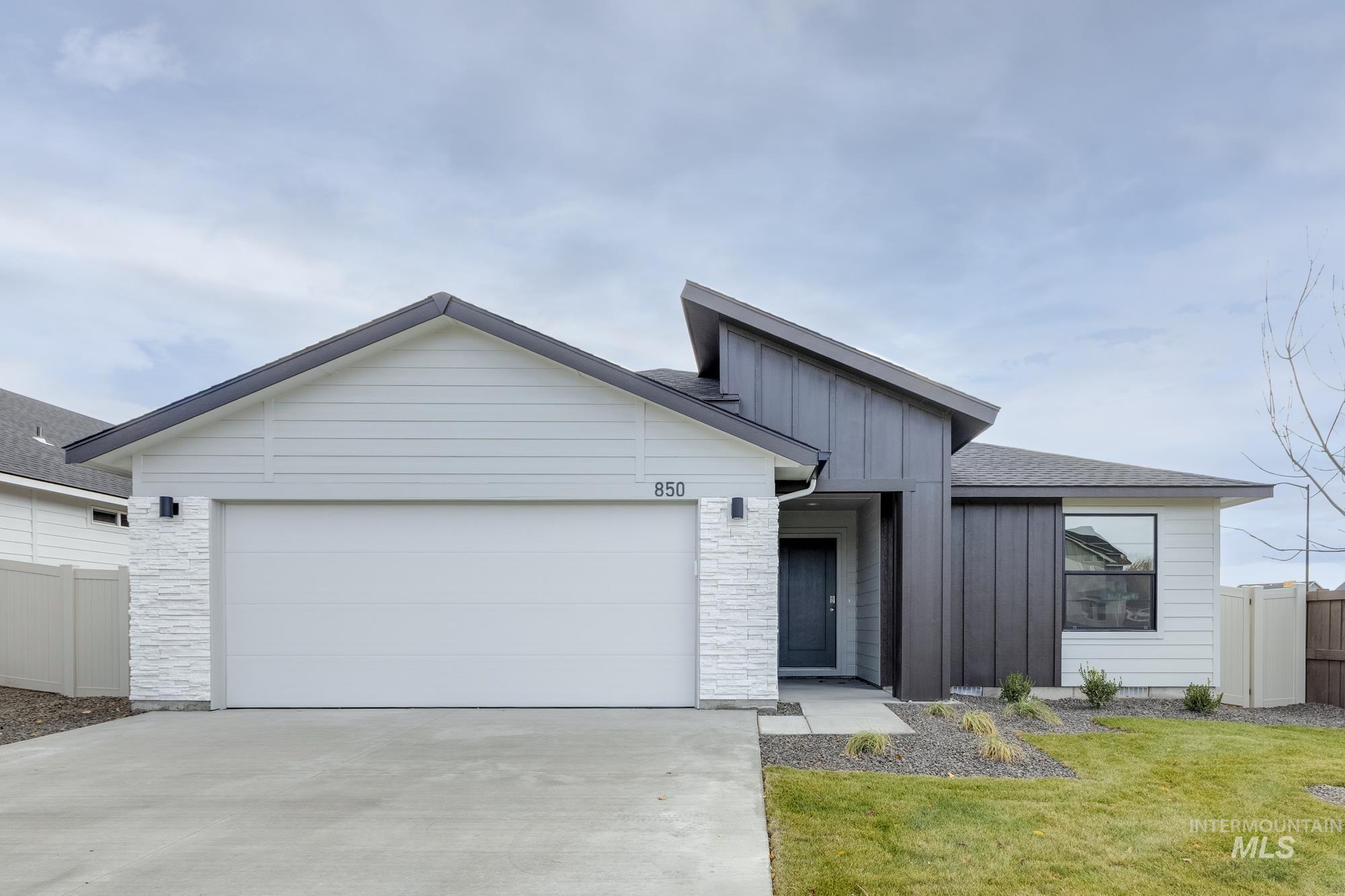 View of front of house with board and batten siding, driveway, stone siding, and a garage