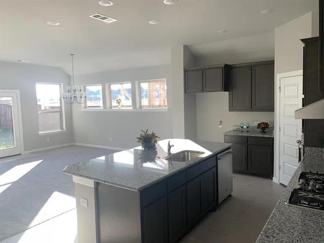 a kitchen with stainless steel appliances granite countertop a sink a stove a refrigerator cabinets and a dining table