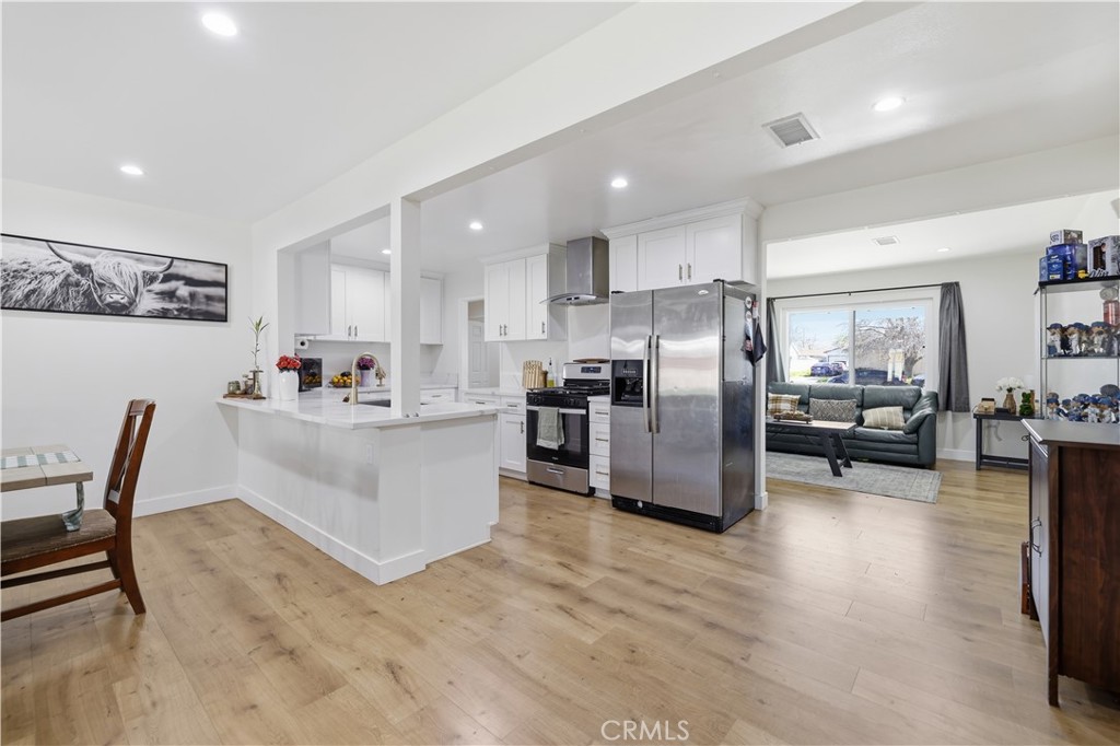 44335 Glenraven Road Lancaster, CA 93535 - Photo 7 of 32 a kitchen with stainless steel appliances kitchen island granite countertop a refrigerator a stove a sink a dining table and chairs with wooden floor