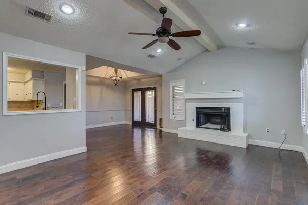 an empty room with wooden floor a ceiling fan a fireplace and windows