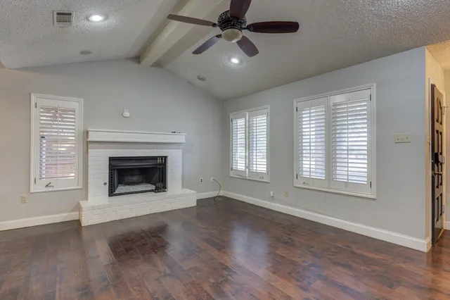 an empty room with wooden floor fireplace and windows