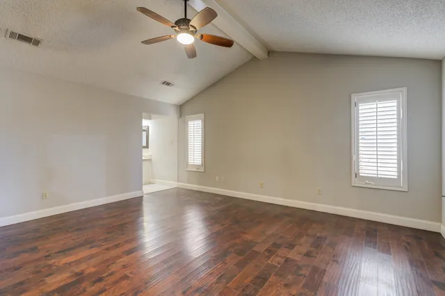 an empty room with wooden floor chandelier fan and windows