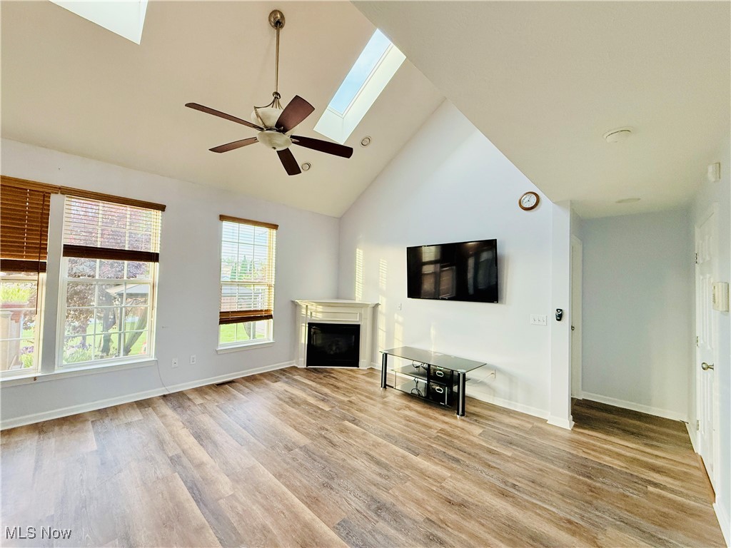 155 Stone Ridge Way Berea, OH 44017 - Photo 10 of 32 Unfurnished living room with a skylight, light wood finished floors, a glass covered fireplace, ceiling fan, and high vaulted ceiling