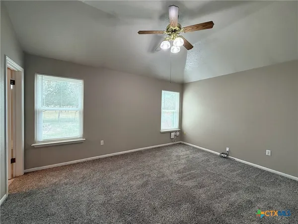 an empty room with a chandelier fan and windows