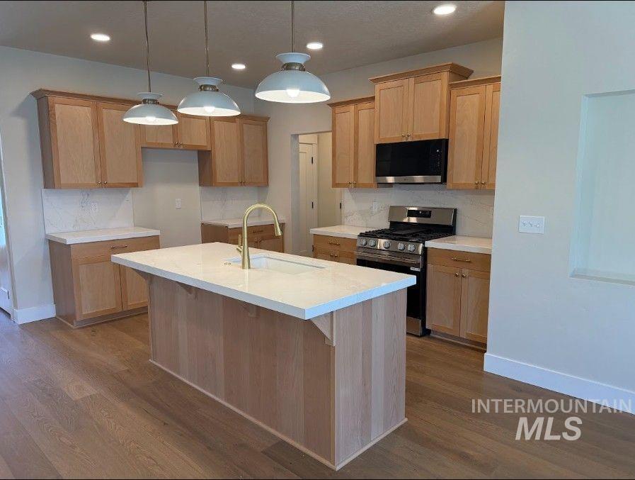 683 West Wrangler Street Meridian, ID 83646 - Photo 6 of 23 Kitchen featuring a central island with an integrated sink, light wood-finish cabinetry, quartz countertops, a modern gas range, and wood-finish flooring