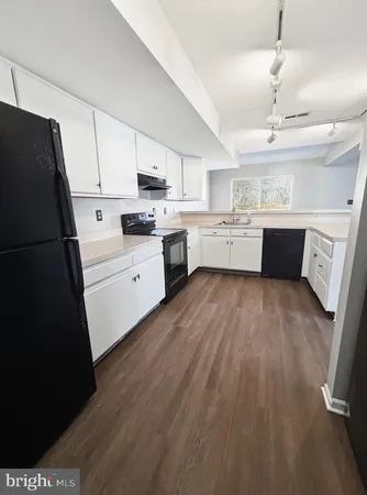 a kitchen with granite countertop a refrigerator a sink dishwasher a stove and white countertops with wooden floor