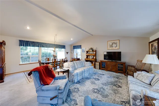 a view of a dining room and livingroom with furniture wooden floor a rug a flat screen tv a painting and a chandelier