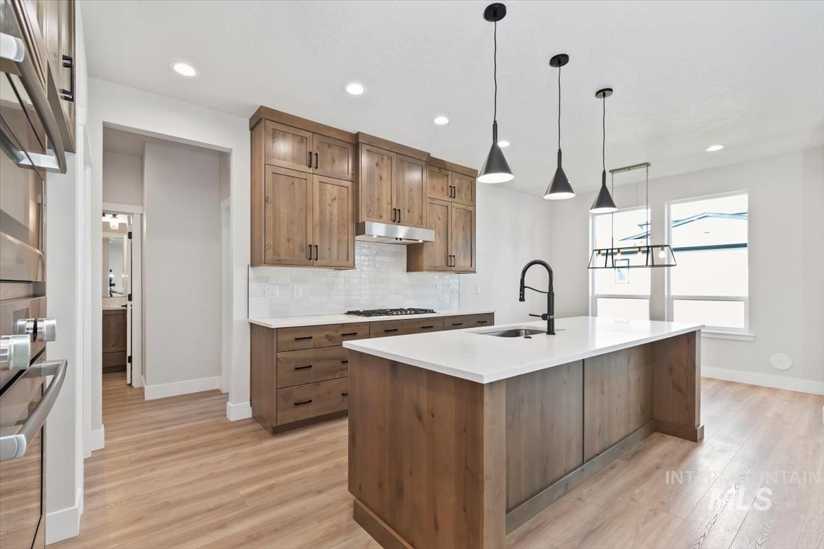 2830 West Jutland Street Meridian, ID 83642 - Photo 11 of 40 Kitchen featuring brown cabinetry, backsplash, hanging light fixtures, light stone countertops, and light wood finished floors