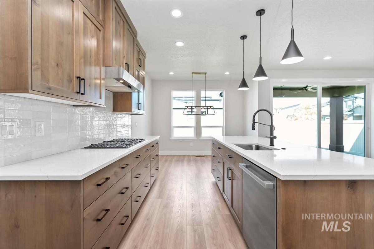 2830 West Jutland Street Meridian, ID 83642 - Photo 12 of 40 Kitchen featuring brown cabinets, hanging light fixtures, stainless steel appliances, a kitchen island with sink, and light stone countertops