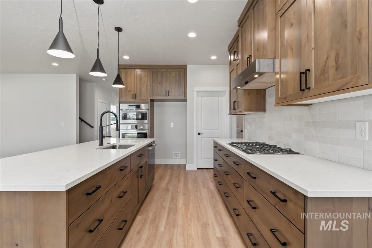 2830 West Jutland Street Meridian, ID 83642 - Photo 7 of 40 Kitchen with brown cabinetry, hanging light fixtures, an island with sink, light stone countertops, and light wood finished floors