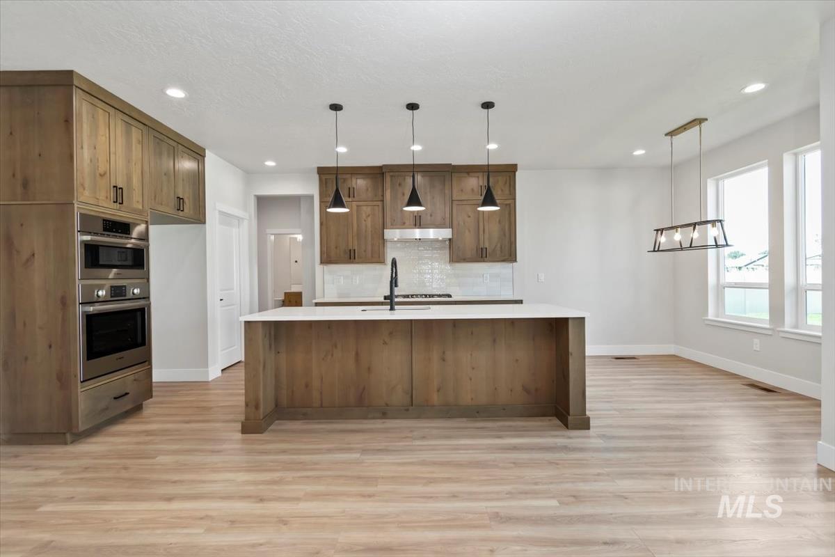 2830 West Jutland Street Meridian, ID 83642 - Photo 8 of 40 Kitchen with backsplash, hanging light fixtures, light stone counters, light wood-style flooring, and recessed lighting