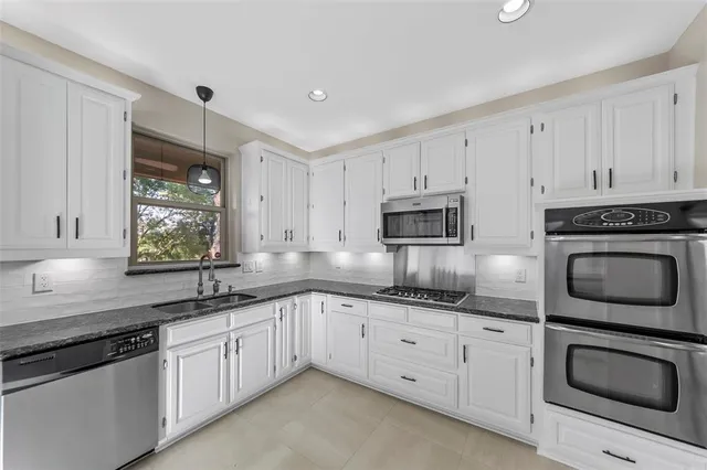 a kitchen with granite countertop white cabinets sink and stainless steel appliances