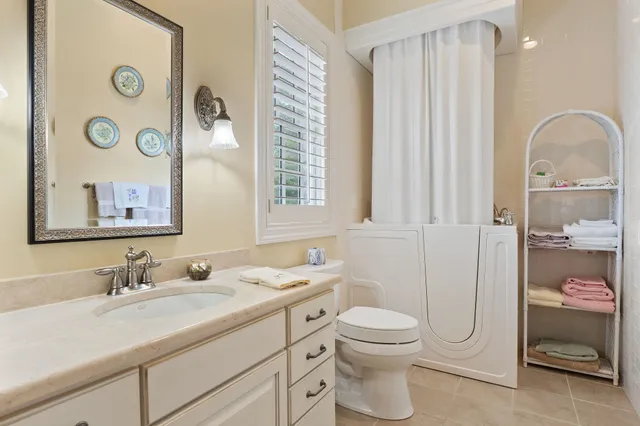 a bathroom with a toilet a sink a glass door a shower a mirror a vanity and window