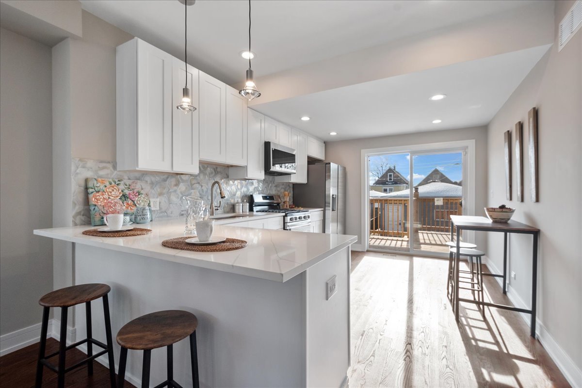 4855 West School Street Chicago, IL 60641 - Photo 11 of 29 a kitchen with stainless steel appliances granite countertop a stove a sink a dining table and chairs with wooden floor