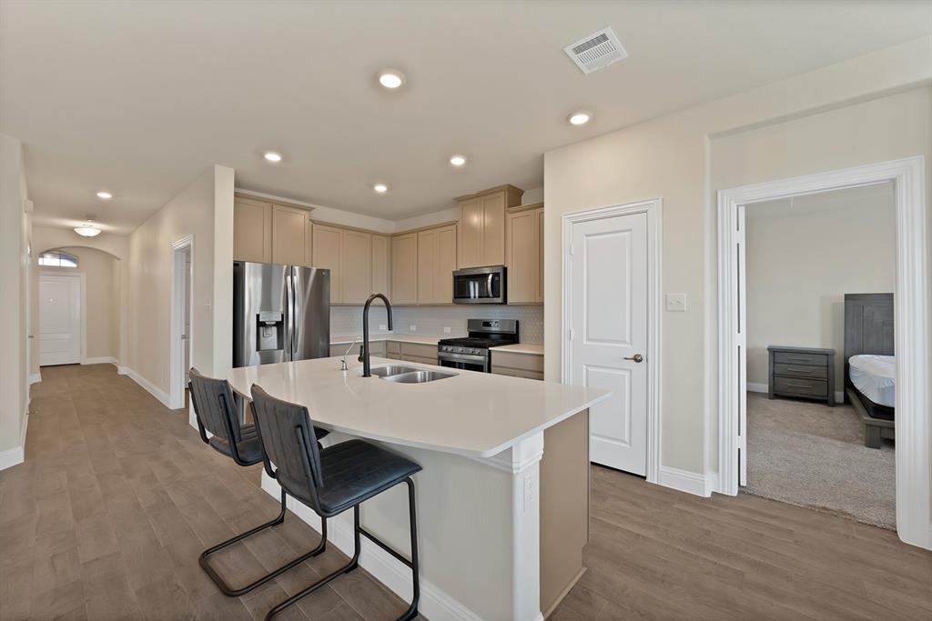 10401 Table Blf Street Aubrey, TX 76227 - Photo 3 of 25 a kitchen with kitchen island a stove a refrigerator and a dining table with wooden floor