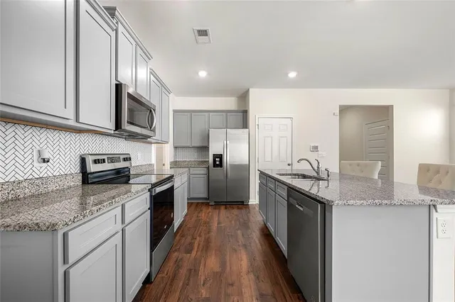 a kitchen with stainless steel appliances granite countertop a stove top oven a sink dishwasher a refrigerator and white cabinets with wooden floor