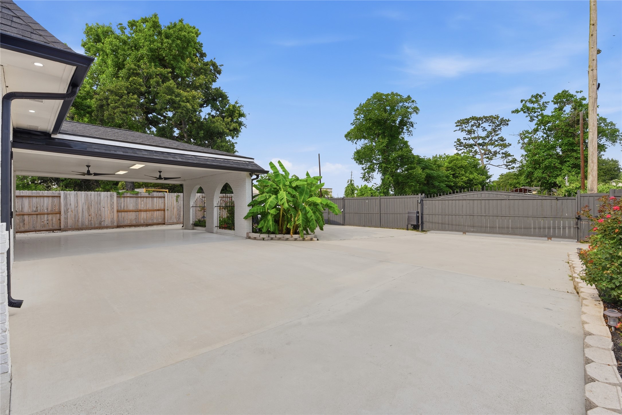 9403 Spaulding Street Houston, TX 77016 - Photo 5 of 50 Spacious outdoor area featuring a covered patio with arched openings and ceiling fans, surrounded by greenery and a secure fence, perfect for entertaining or relaxing.