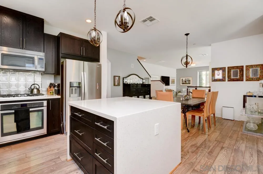 7832 Inception Way San Diego, CA 92108 - Photo 8 of 31 a kitchen with a refrigerator a stove top oven a dining table and chairs with wooden floor