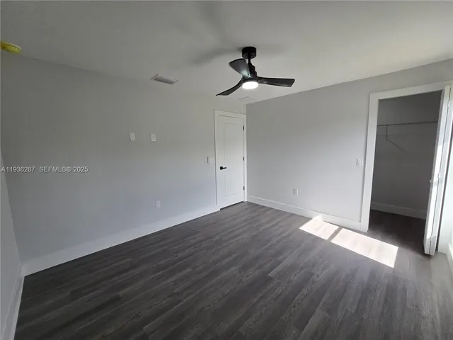 an empty room with wooden floor fan and windows