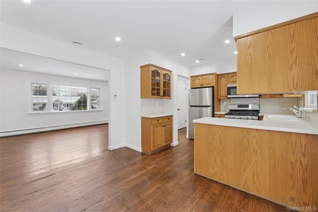 a kitchen with stainless steel appliances granite countertop a stove a sink a refrigerator white cabinets and wooden floor next to a window