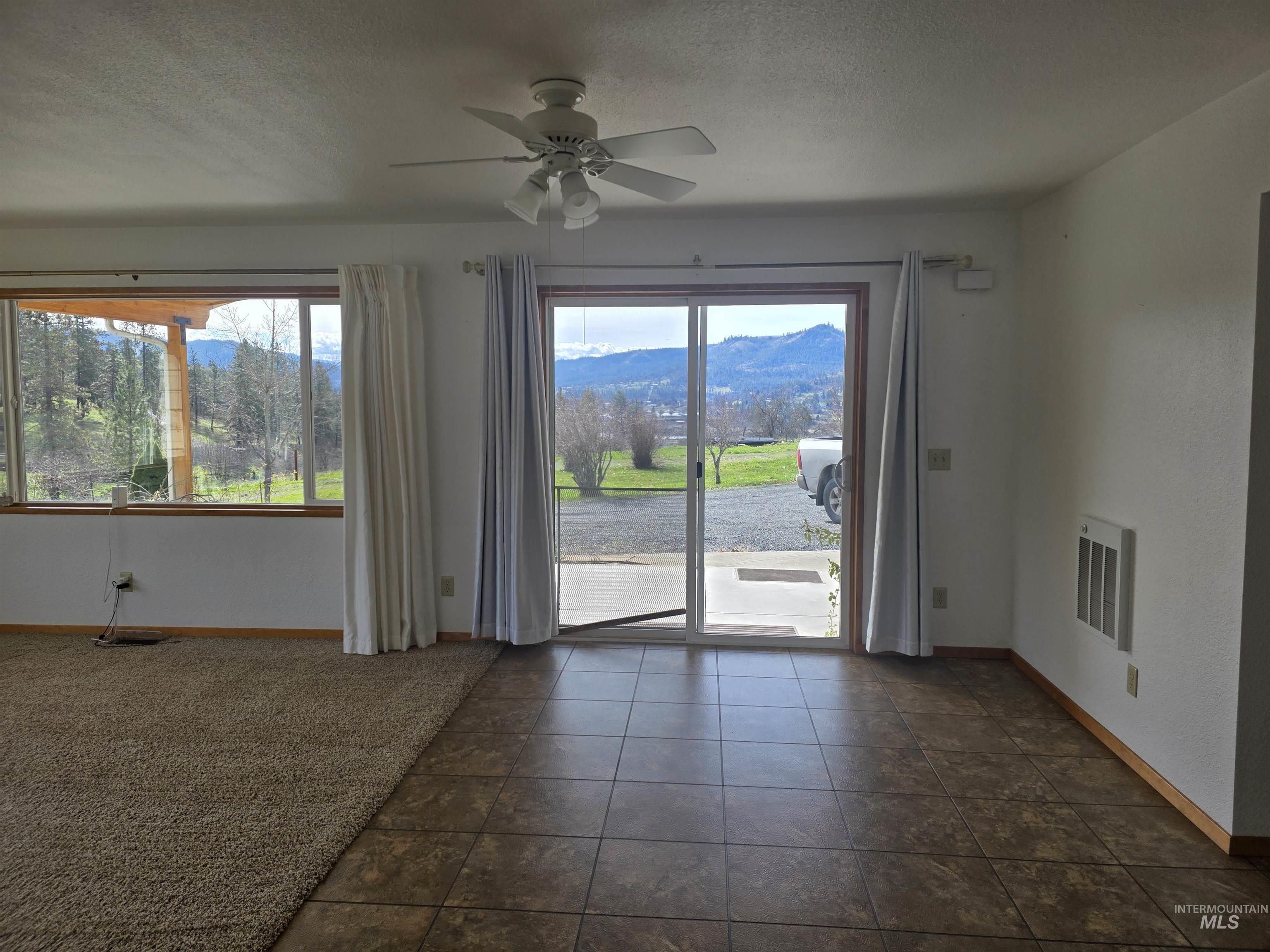 367 Woodland Road Kamiah, ID 83536 - Photo 11 of 45 Empty room with a ceiling fan, a mountain view, a textured ceiling, plenty of natural light, and dark tile patterned flooring