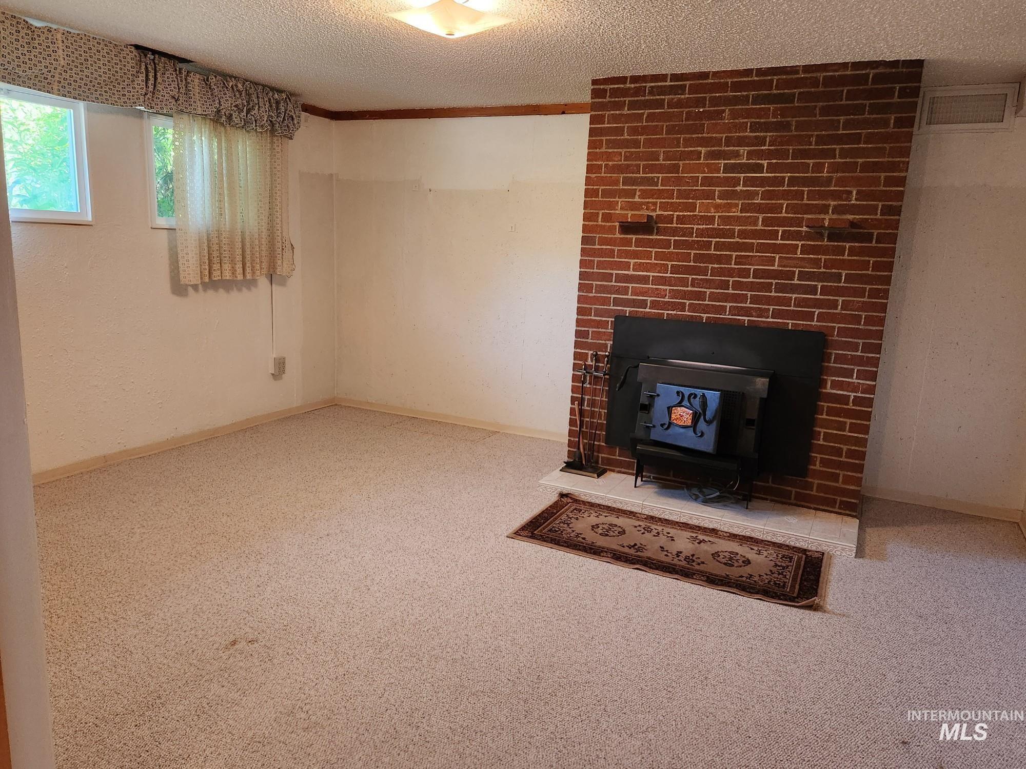 367 Woodland Road Kamiah, ID 83536 - Photo 19 of 45 Unfurnished living room featuring a wood stove, light carpet, a textured ceiling, and crown molding