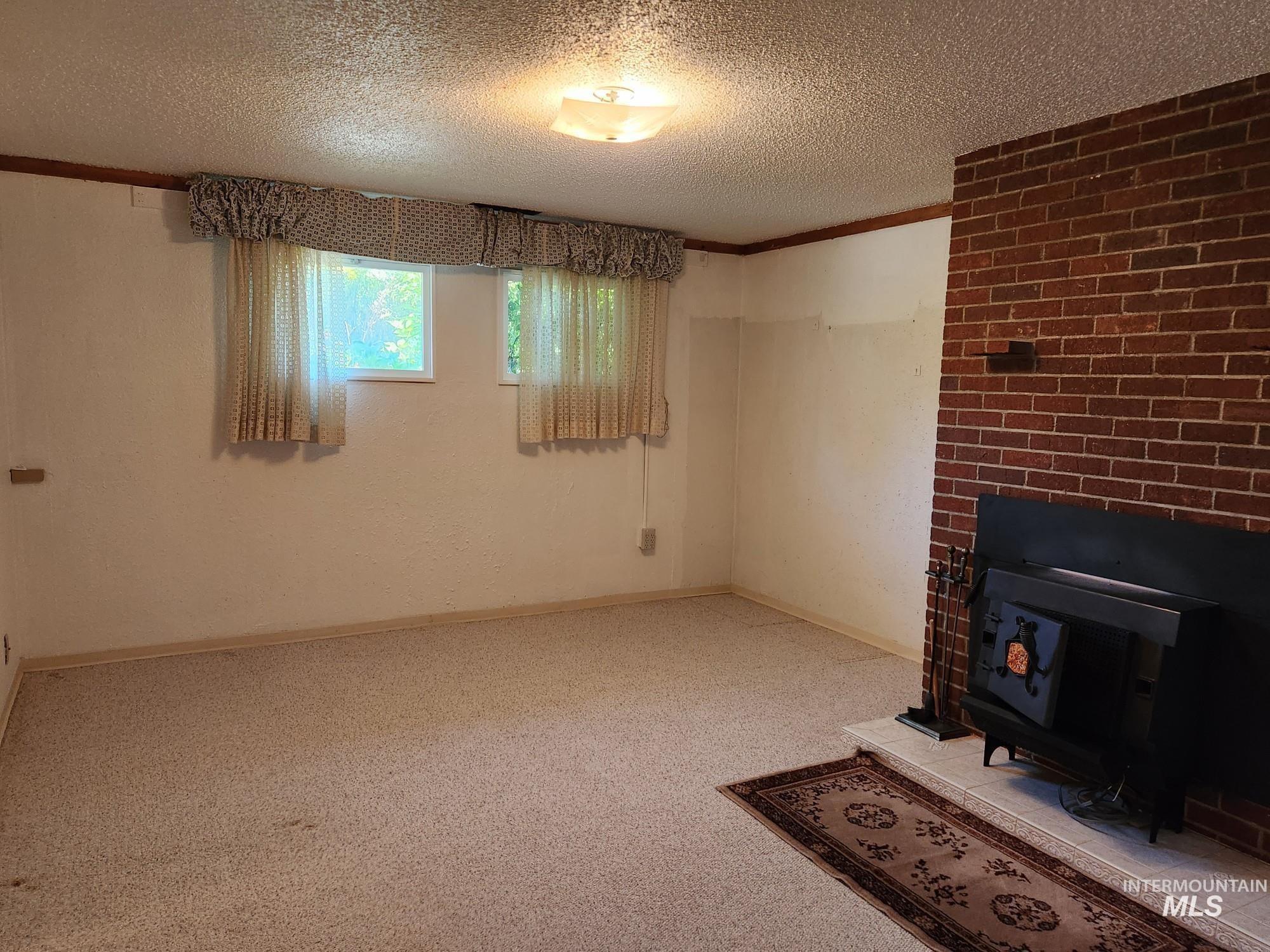 367 Woodland Road Kamiah, ID 83536 - Photo 20 of 45 Unfurnished living room featuring a wood stove, light colored carpet, a textured ceiling, and ornamental molding
