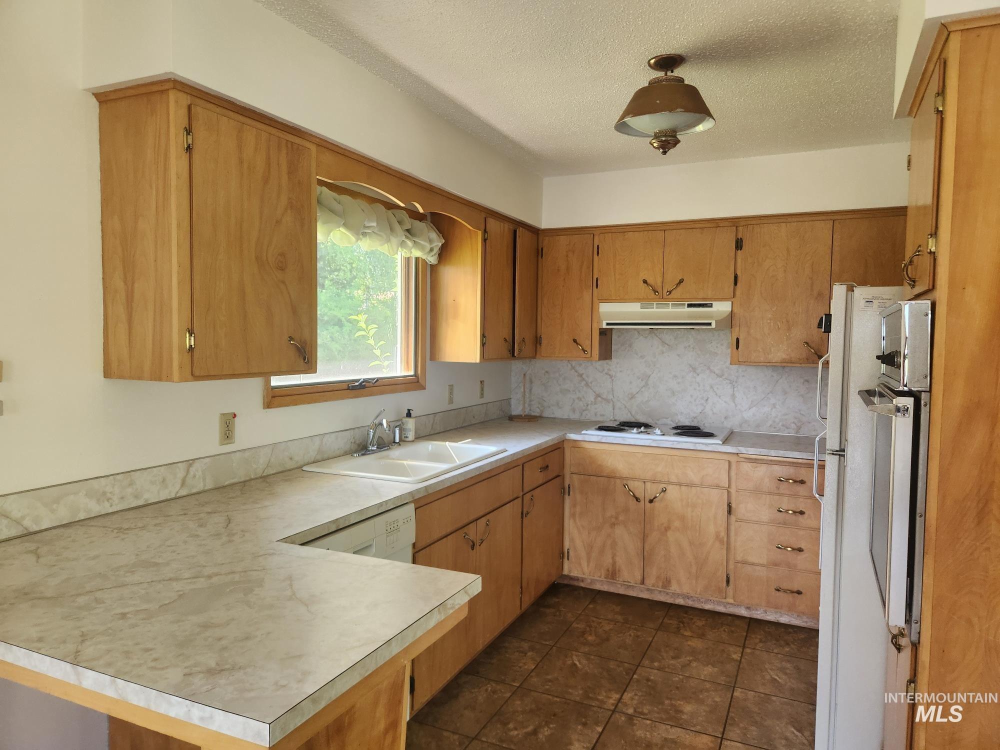 367 Woodland Road Kamiah, ID 83536 - Photo 8 of 45 Kitchen with a peninsula, light countertops, white appliances, backsplash, and a textured ceiling