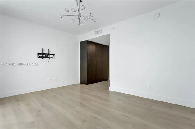 an empty room with a chandelier fan and wooden floor