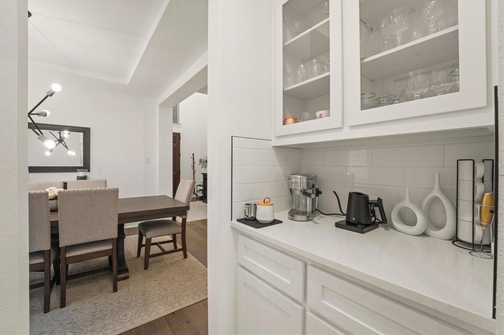 1714 Highwood Road Forney, TX 75126 - Photo 12 of 28 Bar featuring white cabinetry, glass insert cabinets, dark wood finished floors, backsplash, and light stone counters